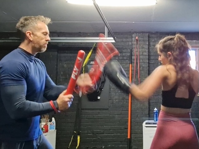 Woman practicing kickboxing techniques with coach holding pads at Boxing Fitness MK