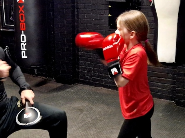 Young girl practicing boxing punches with coach holding pads at Boxing Fitness MK training session